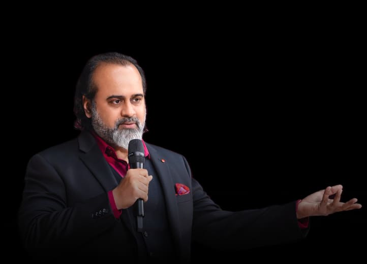 Acharya Prashant speaking into a microphone with his hand extended